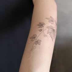 a woman's arm with a vine and leaves tattoo on the left side of her arm