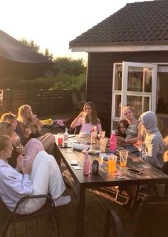 a group of people sitting around a wooden table eating food and drinking beverages on a deck