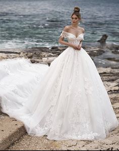 a woman in a white wedding dress standing on rocks near the ocean with her hand on her hip