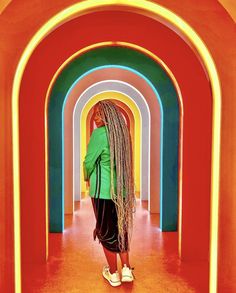 a woman with dreadlocks standing in front of an arch that is painted multicolored