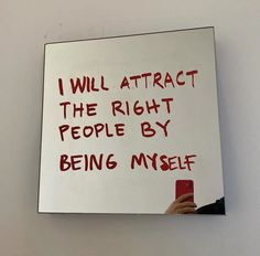 a person holding a cell phone in front of a white board with writing on it that says, i will attract the right people by being my self