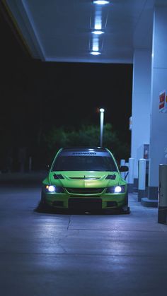 a green car parked in front of a gas station with its lights on at night