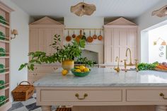 a large kitchen with pink cabinets and marble counter tops is pictured in this image, there's a bowl of lemons on the island