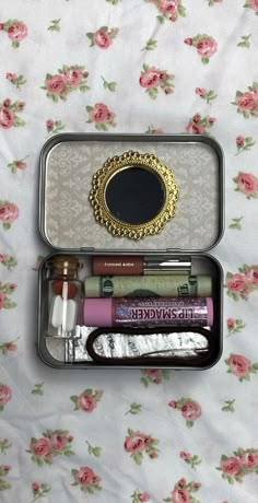 an open tin can with lipstick and other items in it on a floral bed sheet