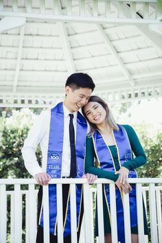 a man and woman standing next to each other in front of a white fence with trees