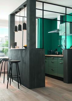 an open kitchen with green walls and stools next to the counter top, along with two bar stools