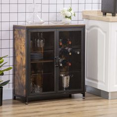 a cabinet that is next to a counter with wine glasses on it and a potted plant in the corner