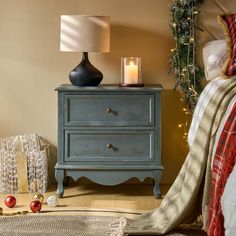 a night stand with a lit candle on it next to a bed and christmas decorations