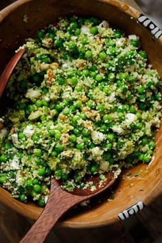 a wooden spoon in a bowl filled with peas and feta on top of a table