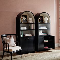 two black bookshelves with arched glass doors in front of a pink painted wall