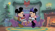 two mickey mouses sitting on a couch in front of a christmas tree and fireplace