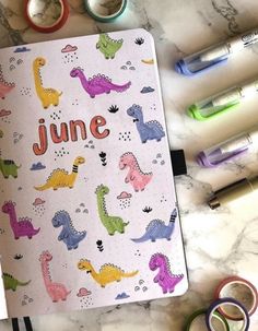 an open notebook with dinosaurs on it next to markers, pens and washables