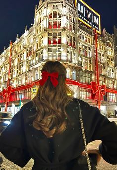 a woman standing in front of a building with a red bow on her head and long hair