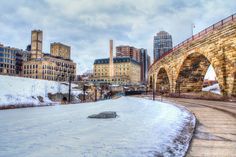 an old stone bridge over a frozen river with snow on the ground and buildings in the background