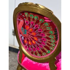 a pink and gold chair with a peacock design on it's backrest, in front of a white door