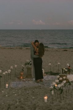 a couple embracing each other on the beach with candles in front of them and flowers all around