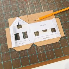 paper cut out to look like a house with two windows on it and a pencil next to it