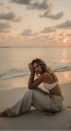 a woman is sitting on the beach with her hand in her ear and looking into the distance