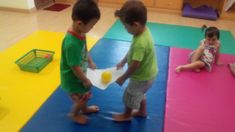 two young children playing with a ball on the floor in a play room at a school