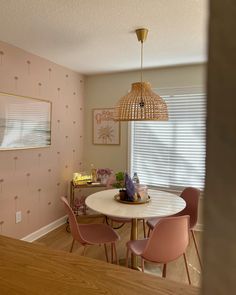 a dining room with pink chairs and a white table in front of a wallpapered window