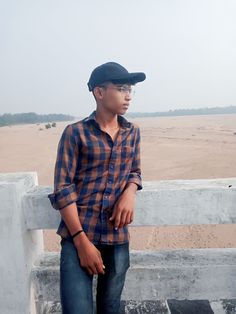 a young man standing on top of a wooden fence next to a sandy beach in the distance