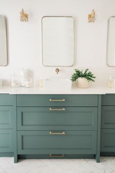 a bathroom with green cabinets and two mirrors above the sinks, along with a plant