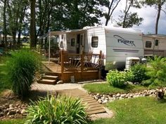 a trailer parked in the grass next to some trees and bushes with stairs leading up to it