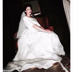 a woman in a white wedding dress sitting on a chair with her arm around the neck