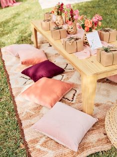 a picnic table with boxes and flowers on it, sitting in the grass next to some pillows