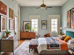 a bedroom with blue walls and pictures on the wall above the bed, along with two windows