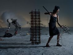 a woman holding a baseball bat standing on top of a sandy beach next to a pile of junk