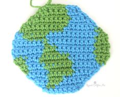 a crocheted earth ornament hanging on a white surface with green and blue yarn