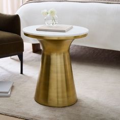 a white and gold side table with flowers on it in a bedroom setting next to a bed