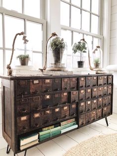 an old dresser with many drawers and plants on top, in front of a window