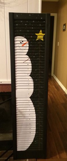 a snowman made out of shutters on top of a wooden floor next to a door