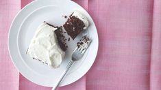 a piece of cake on a white plate with a fork and pink table cloth behind it