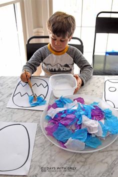 a young boy sitting at a table with paper cut out of the shape of batmans