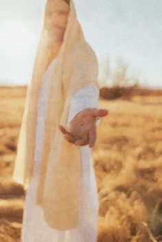 a woman in a white robe holding her hand out to the side while standing in a field