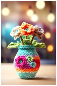 a crocheted vase with flowers in it sitting on a table next to a blurry background