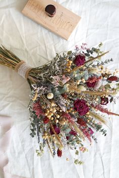 dried flowers are laid out on a white sheet with a bottle of wine in the background