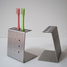 two toothbrushes are in a metal holder on a white counter top, one is pink and the other is green