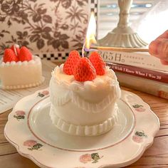 a white cake with strawberries on top sitting on a plate next to a candle