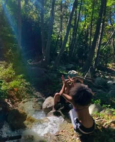 a woman sitting on top of a rock next to a forest filled with trees and water