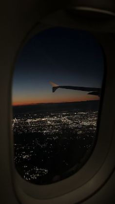 an airplane window looking out at the city lights and sky from inside another plane's wing