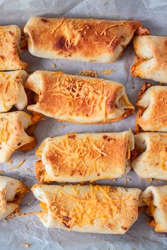 several cheesy bread rolls are lined up on a sheet of wax paper with shredded cheese