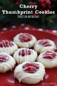 cherry thumbprint cookies with white icing on a red plate next to holly branches