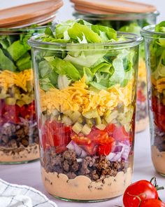 three mason jars filled with salad ingredients and topped with lettuce, tomatoes, cheese, and other toppings