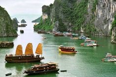 several boats floating in the water near mountains and cliffs on a cloudy day with yellow sails