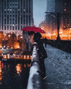 a woman with an umbrella is standing on the sidewalk in the rain at night time