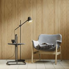 a chair with a pillow on it next to a lamp and table in front of a wooden wall